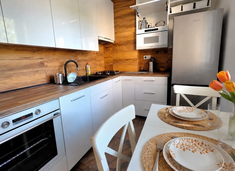Küche in einer 2-Zimmer-Wohnung mit weißen Schränken, Holzboden und einem Tisch mit Blumen.