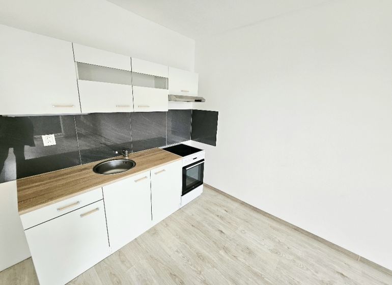Weiße Küchenzeile mit schwarzer Verkleidung in einer Einzimmerwohnung mit Holzboden.