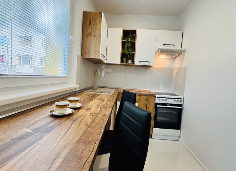 Küche in einer Einzimmerwohnung mit Holzboden, weißen Schränken und Geräten.
