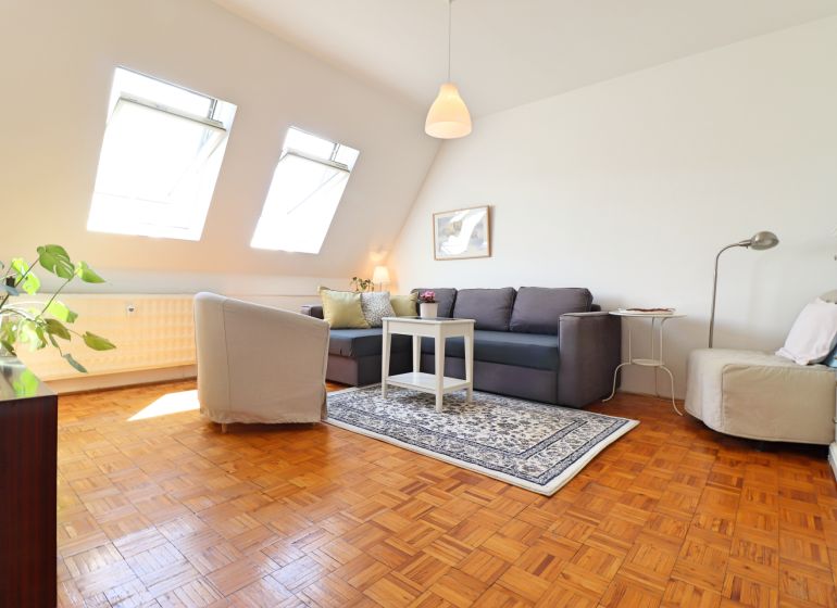 Wohnzimmer in einer 2-Zimmer-Wohnung mit Holzboden und hellen Dachfenstern.