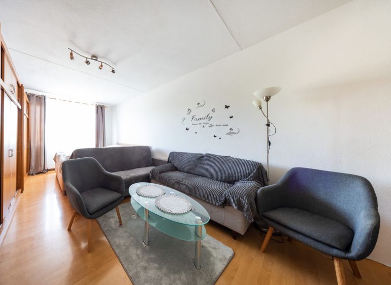 Wohnzimmer mit Holzboden in einer 3-Zimmer-Wohnung, graue Sofas, Glastisch.