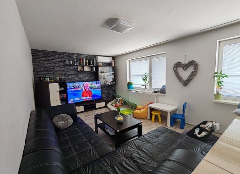 Wohnzimmer in einer 3-Zimmer-Wohnung mit Sofa und Fernseher, Boden mit Holzdekor.
