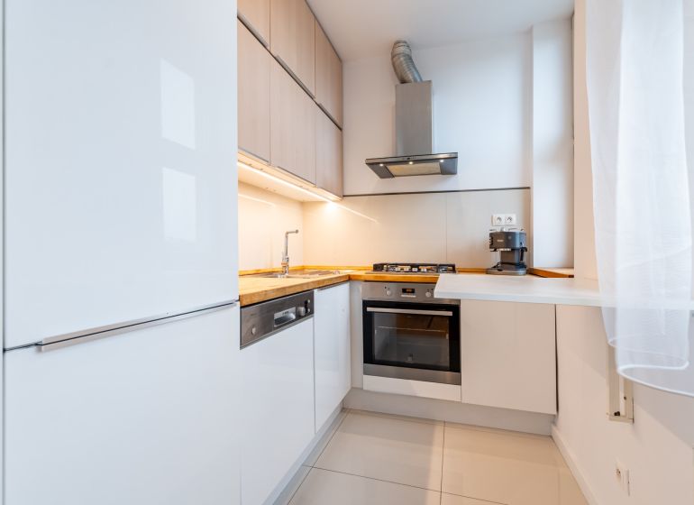 Helle Küche in einer Zweizimmerwohnung mit weißen Schränken und Holzelementen.