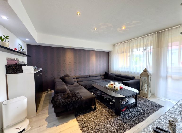 Wohnzimmer in einer 4-Zimmer-Wohnung mit einem dunklen Sofa, einem Boden mit Holzdekor und Dekorationen.