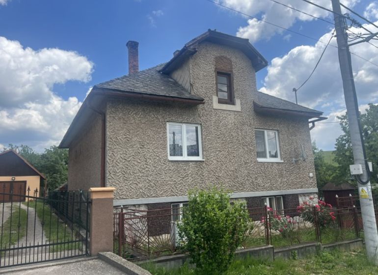 Ein Einfamilienhaus in Rudná mit einer zweistöckigen Fassade, einem eingezäunten Grundstück und blauem Himmel.