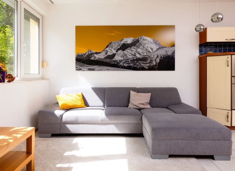 Wohnzimmer in einer 2-Zimmer-Wohnung, graues Sofa, Bild von Bergen, helle Wände.