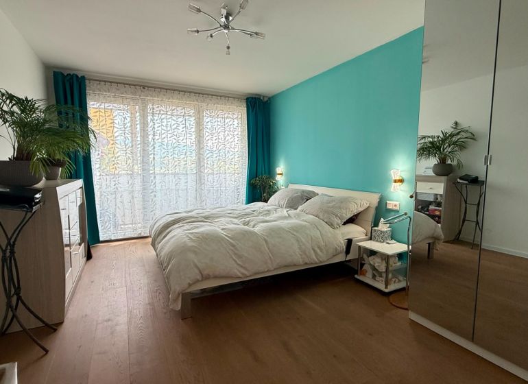 Helles Schlafzimmer mit türkisfarbener Wand, Holzboden und Spiegelschrank in einer Vierzimmerwohnung.