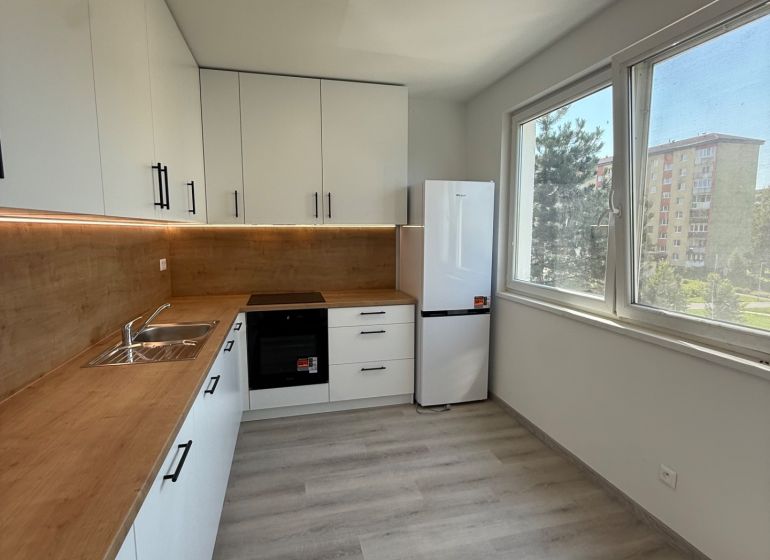 Küche in einer 3-Zimmer-Wohnung mit weißen Schränken und einem Boden in Holzoptik.