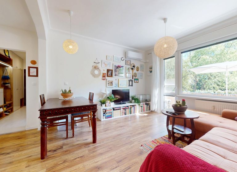 Wohnzimmer in einer 3-Zimmer-Wohnung mit Holzboden, großem Fenster und dekorativen Elementen.