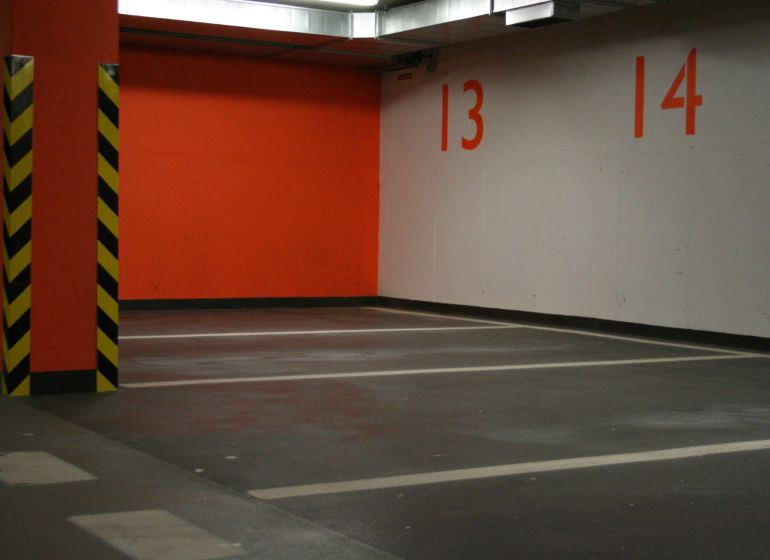 Parkplätze und eine orangefarbene Wand in der Garage mit gelben und schwarzen Säulen.