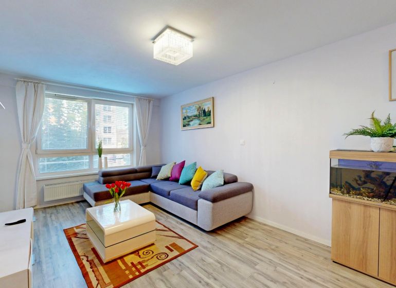 Wohnzimmer in einer 3-Zimmer-Wohnung mit Sofa, Aquarium, Pflanze und Holzboden.
