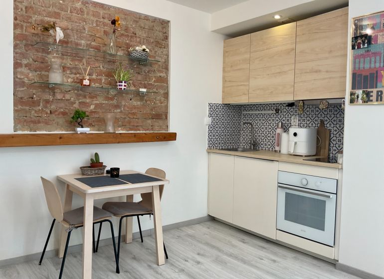 Küchenecke mit einer Ziegelwand und einem Boden in Holzoptik in einer Einzimmerwohnung.