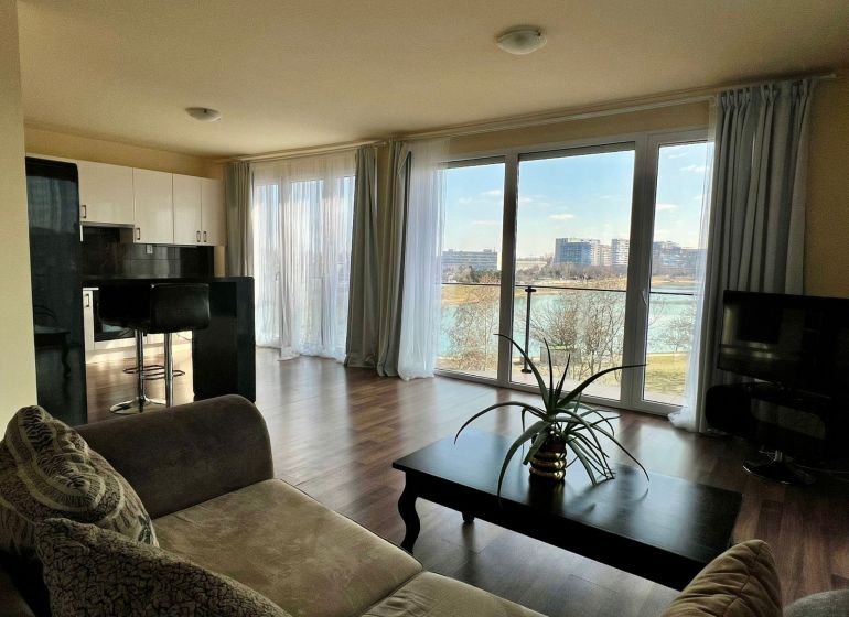 Wohnzimmer in einer 2-Zimmer-Wohnung mit großen Fenstern und einem Boden in Holzoptik.