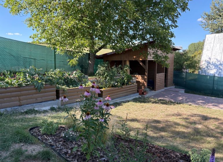 Gärten in Zvolen mit hölzernen Beeten und einem Pavillon, umgeben von Grün und Blumen.