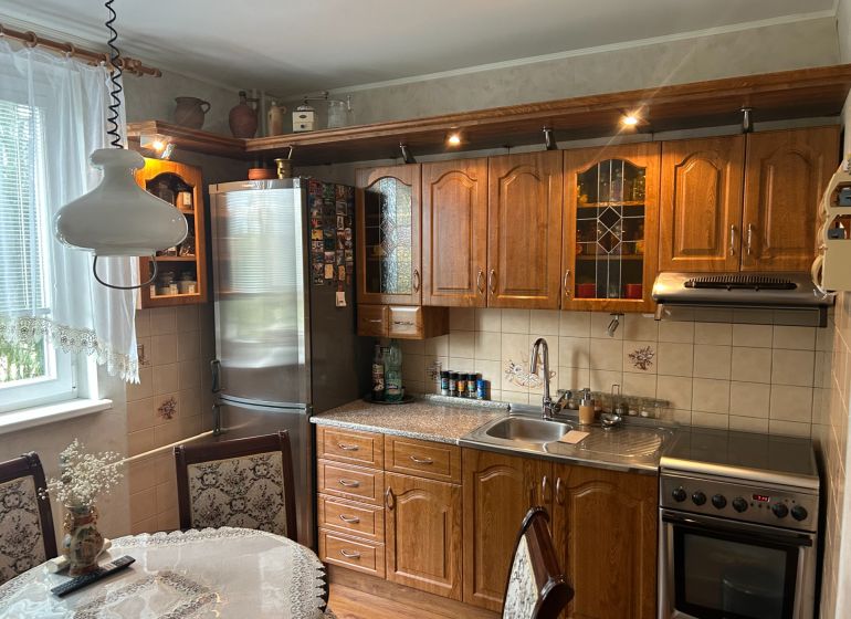 Küche in einer 3-Zimmer-Wohnung mit Holzmöbeln, dekorativem Vorhang und Esstisch.