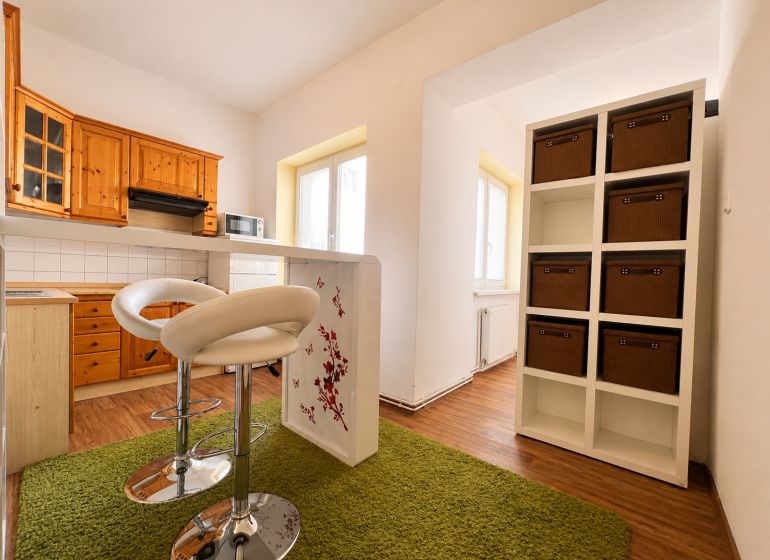 Küche in einer Einzimmerwohnung mit Schränken, Barhockern und einem Boden in Holzoptik.