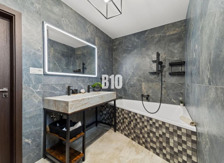 Badezimmer in einem Einfamilienhaus mit Badewanne, Steinverkleidung und großem Spiegel.