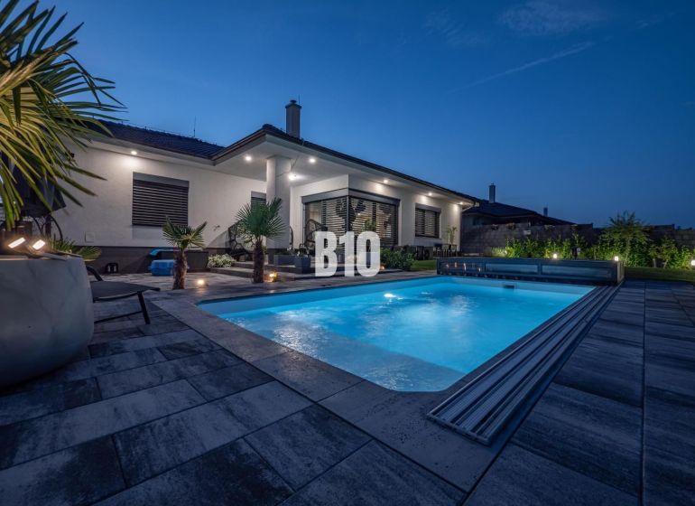 Ein Einfamilienhaus in Nitra mit Pool und Gartenmöbeln in abendlicher Atmosphäre.