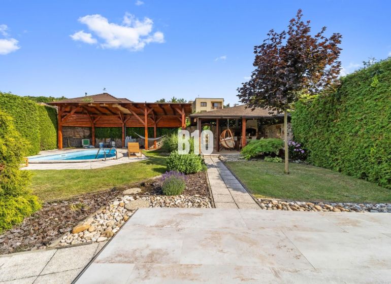 Der Garten eines Einfamilienhauses in Nitra mit einem Pool und einem Pavillon, umgeben von Grün.