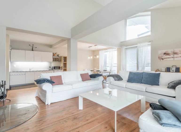 Heller Wohnbereich mit Kamin, Sofas, Küche und Holzboden in einer Ferienwohnung.