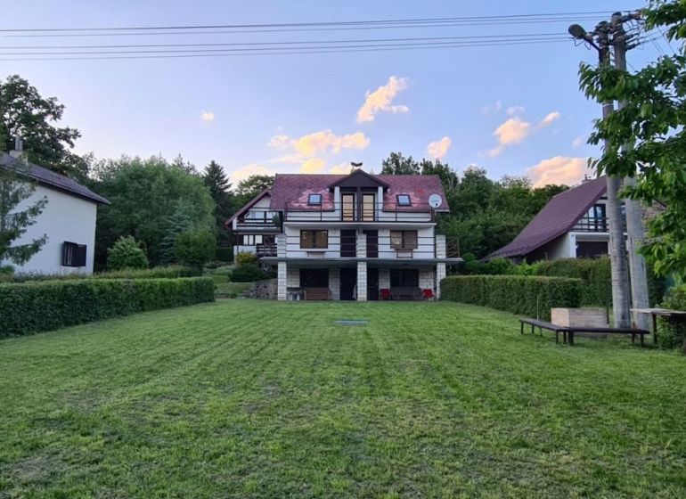 Eine Hütte in Kaluža, umgeben von Grün, gepflegter Rasen, Umgebung mit Bäumen, blauer Himmel.