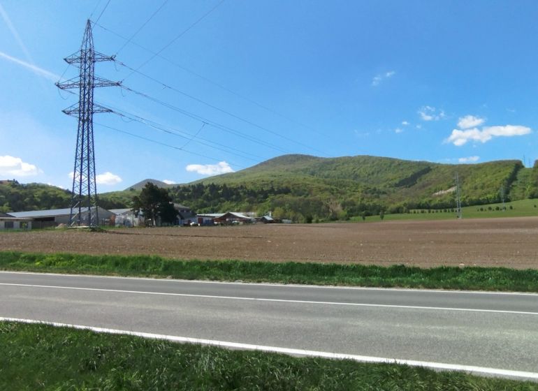 Landschaft an der Továrenská in Smolenice mit landwirtschaftlichen und forstwirtschaftlichen Flächen und Stromleitungen.