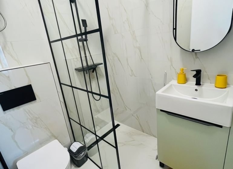 Badezimmer in einer 2-Zimmer-Wohnung mit Duschkabine, Hänge-WC und orangem Teppich.