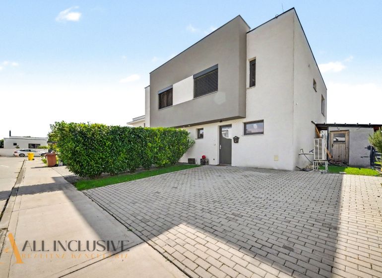 Ein Einfamilienhaus in Hrubá Borša mit gepflastertem Parkplatz und gepflegtem Grünbereich.