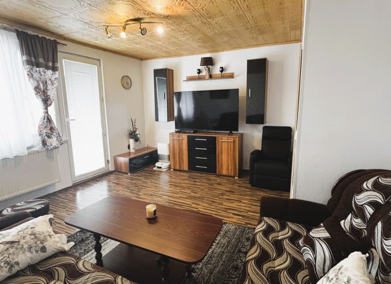 Wohnzimmer in einer 4-Zimmer-Wohnung mit Holzboden und einem Fernseher an der Wand.