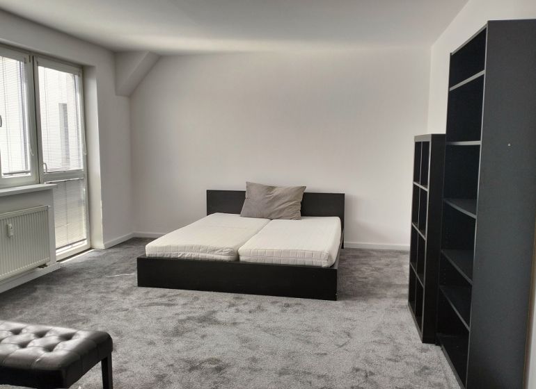 Schlafzimmer in einer 2-Zimmer-Wohnung mit Bett, Regalen und Teppich in neutralen Farben.