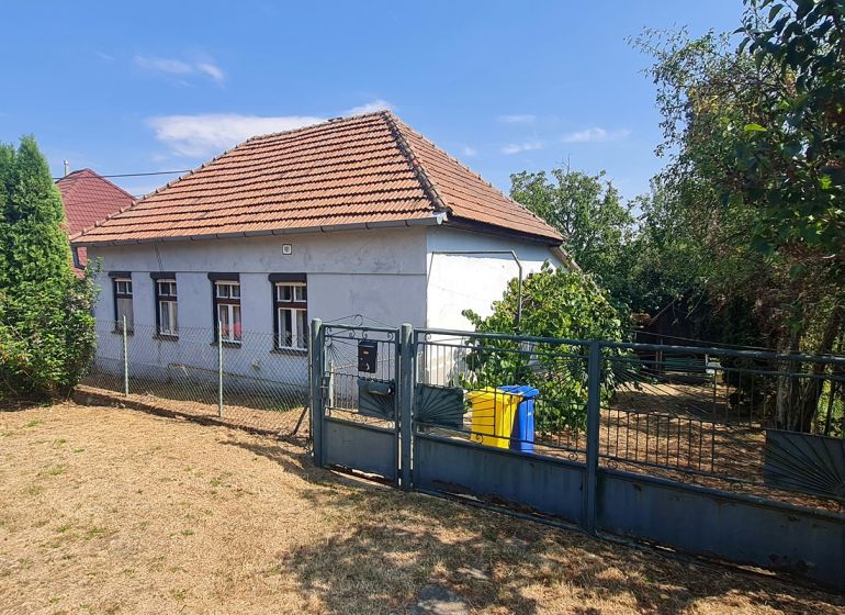 Ein Einfamilienhaus in Dolné Otrokovce mit einem Zaun und einem Garten auf einem sonnigen Grundstück.