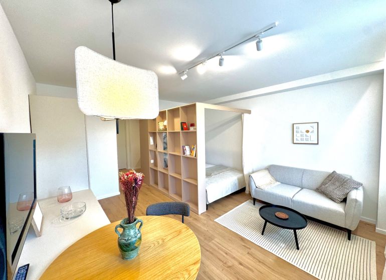 Wohnzimmer mit Holzboden, heller Couch und Esstisch in einer Einzimmerwohnung.