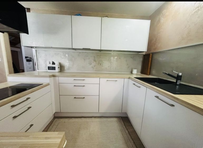 Küche in einer 3-Zimmer-Wohnung mit weißen Schränken und einer Arbeitsplatte in Holzoptik.