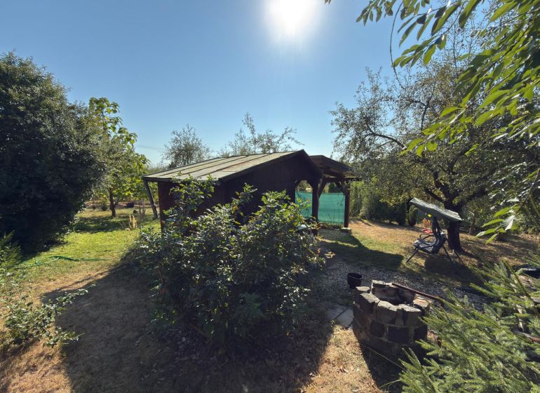Die Hütte im Weingarten in Lučenec, umgeben von Grün und Bäumen, mit einer Feuerstelle im Garten.