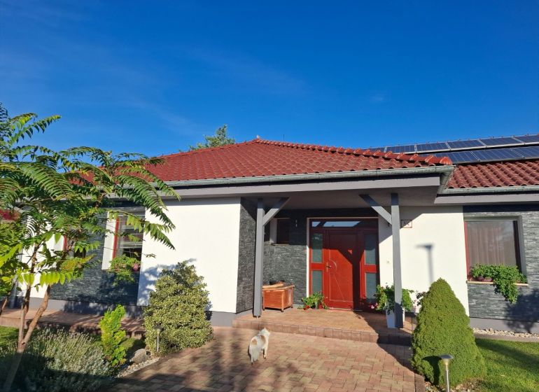 Ein Einfamilienhaus in Nové Zámky mit rotem Dach, Solarpaneelen und Garten.