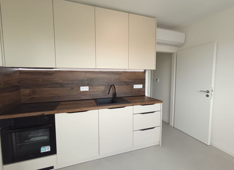 Küche in einer 2-Zimmer-Wohnung mit weißen Schränken und Holzboden.