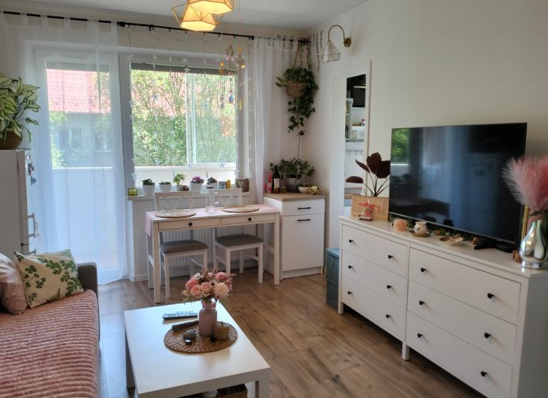 Wohnzimmer in einer Einzimmerwohnung mit Holzboden und weißen Möbeln.