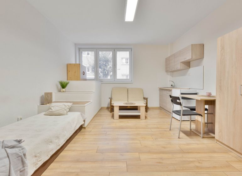 Einzimmerwohnung mit Holzboden, Bett, Kochnische und Möbeln.