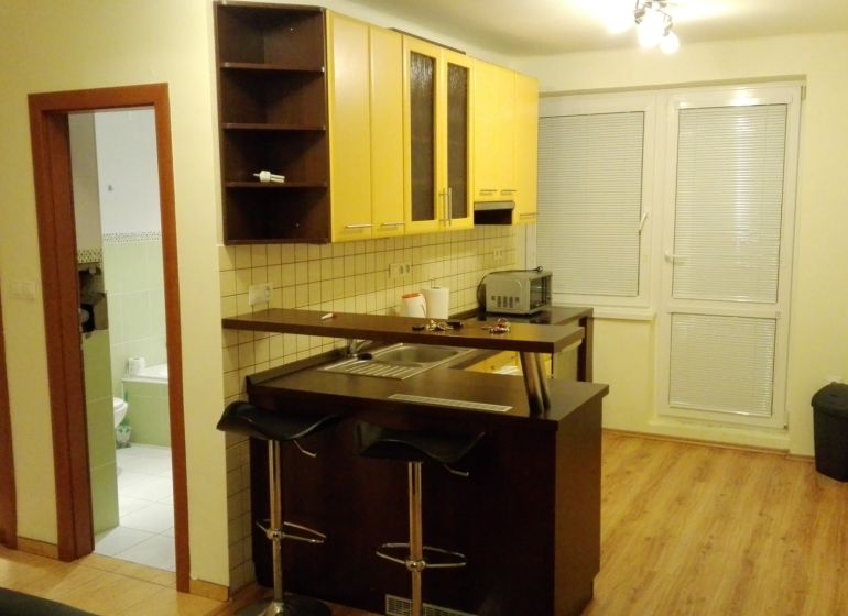 Küchenecke mit gelben Schränken und Theke in einer 3-Zimmer-Wohnung, Boden mit Holzdekor.