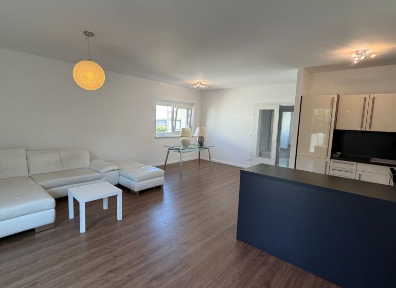 Wohnzimmer in einer 3-Zimmer-Wohnung mit weißem Sofa und Boden in Holzoptik.