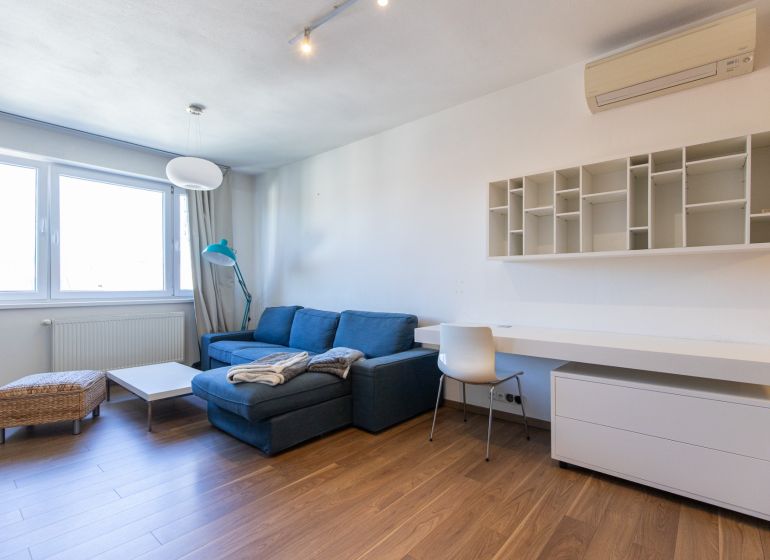 Wohnzimmer mit blauem Sofa, Tisch und Holzboden in einer Einzimmerwohnung.
