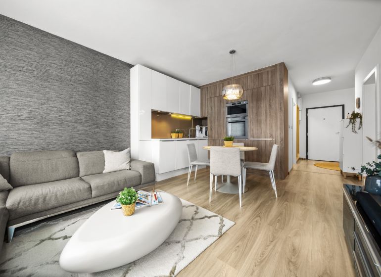 Wohnzimmer in einer Zweizimmerwohnung mit Sofa und Küchenzeile, Holzboden.