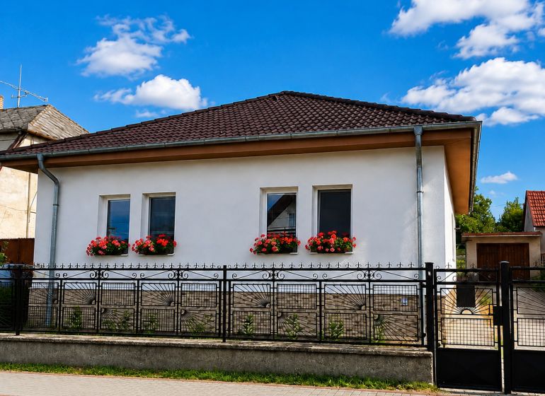 Ein Einfamilienhaus in Šalgočka mit weißer Fassade, Fensterblumen und einem Walmdach.