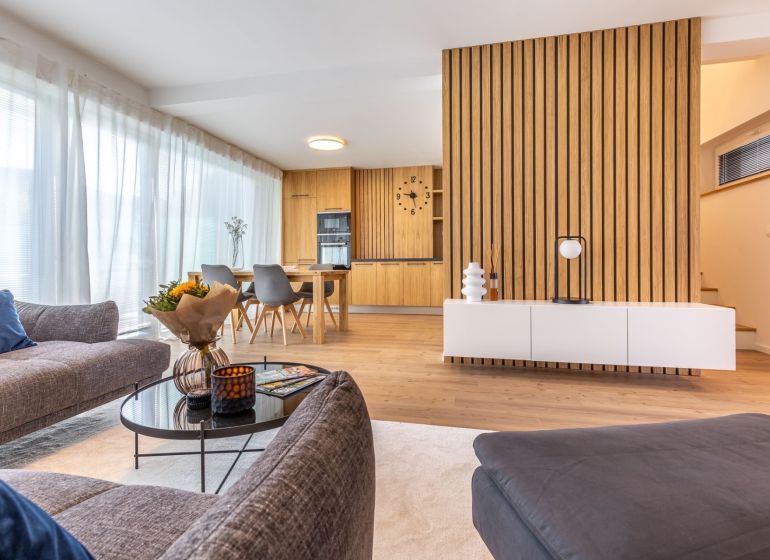 Wohnzimmer in einem Einfamilienhaus mit Holzboden und Essbereich im Hintergrund.