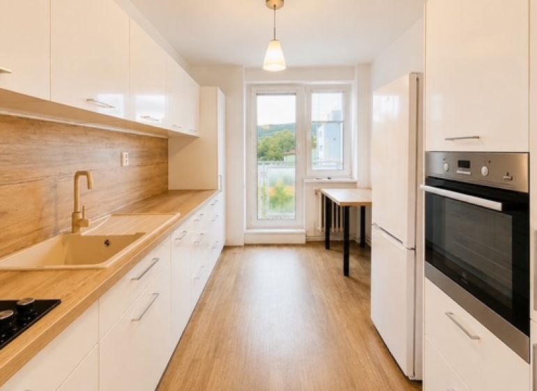 Eine Küche in einer 3-Zimmer-Wohnung mit einem Boden in Holzoptik, einer weißen Küchenzeile und einem Ofen.