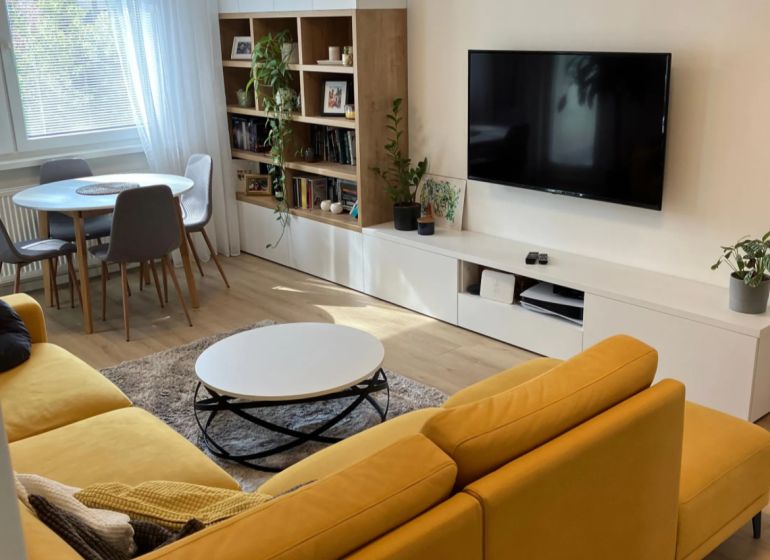 Wohnzimmer in einer 3-Zimmer-Wohnung mit einem bequemen Sofa, einem Esstisch und einem Boden in Holzoptik.