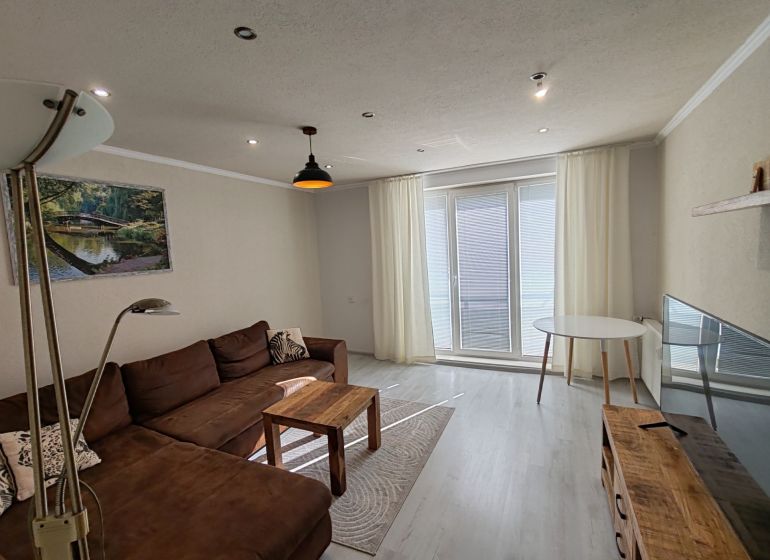 Wohnzimmer in einer 3-Zimmer-Wohnung mit Holzboden und braunem Sofa.