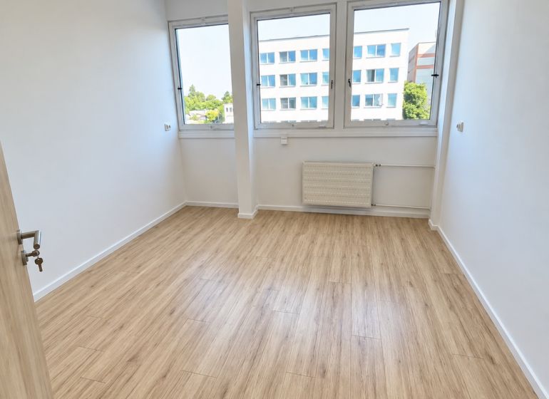 Ein Büro mit einem Boden in Holzoptik, Innenraum mit großen Fenstern und Deckenbeleuchtung.
