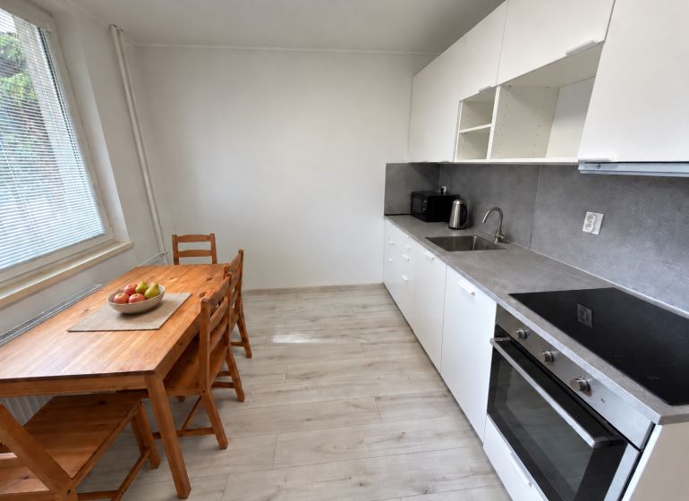 Küche in einer 2-Zimmer-Wohnung mit weißer Küchenzeile und Boden in Holzoptik.