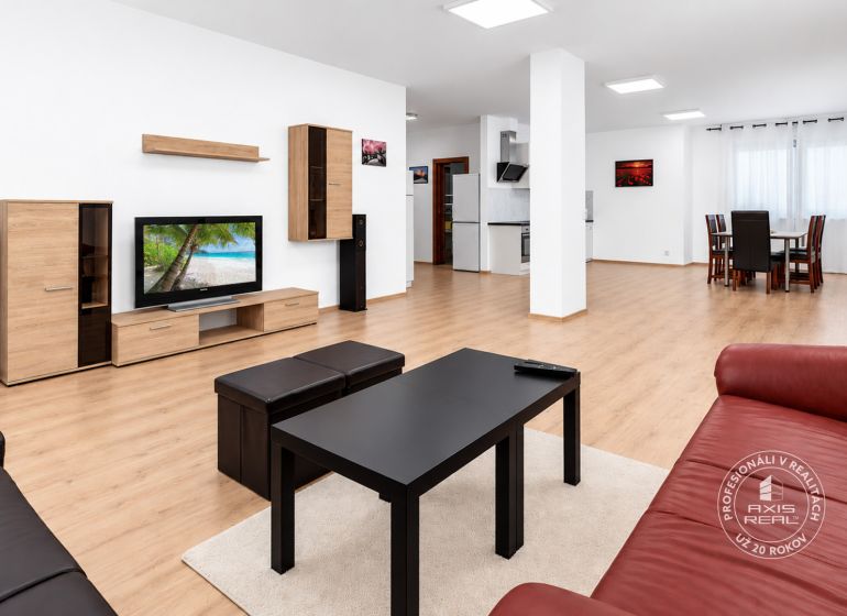 Ein geräumiges Wohnzimmer mit einem roten Sofa, einem Fernseher und einem Boden in Holzoptik.